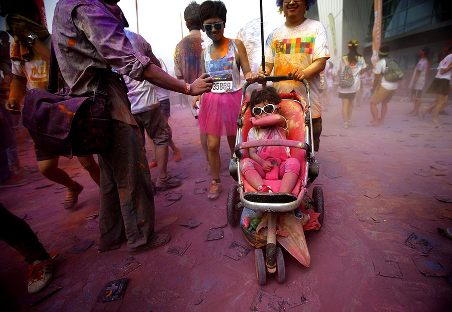 Girl in a stroller covers her mouth as she is pushed across the finish line during the Color Run in Shanghai